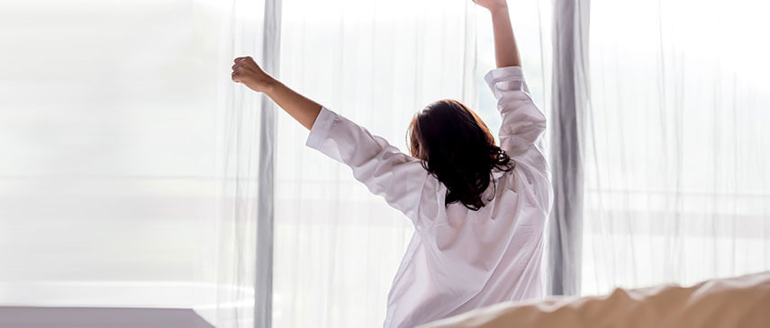 Woman stretching as she wakes up in a sunlit room, starting her morning routines.