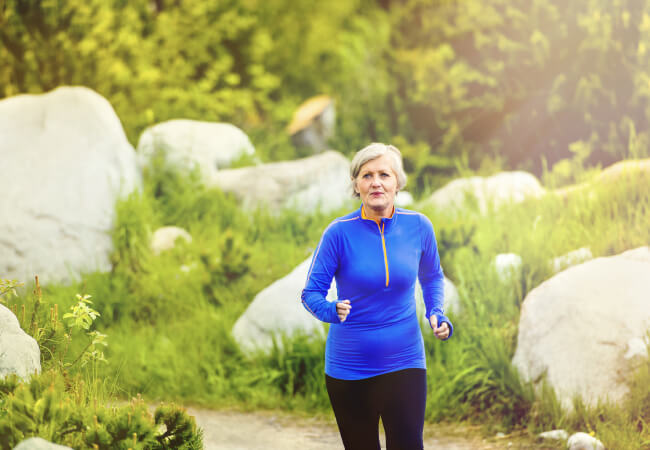 Senior woman with back pain jogging in a park.