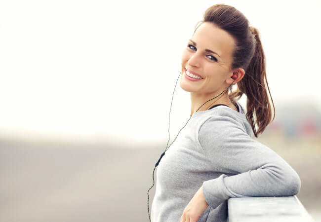 A smiling woman with earphones looking over her shoulder, unaware of the pain origins in her posture.