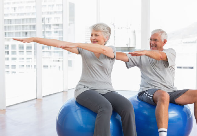 Senior couple exercising with fitness balls in a bright room for arthritis pain relief.