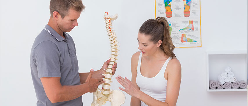 Physical therapist explaining spinal anatomy and hip pain management to a patient in a clinic.