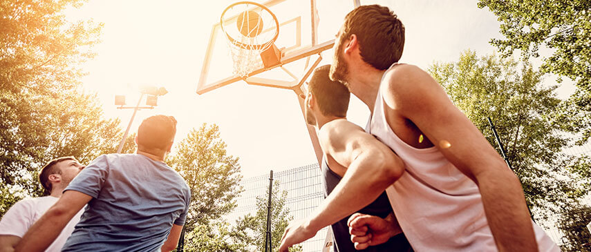 Group of young adults quickly playing basketball outdoors on a sunny day.