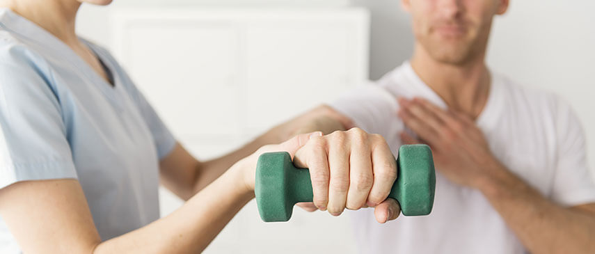 Physical therapist assisting a male patient with his morning routine arm exercise using a dumbbell.