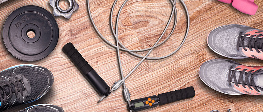 Various workout equipment on a wooden floor, including a jump rope, dumbbells, a weight plate, and sneakers.