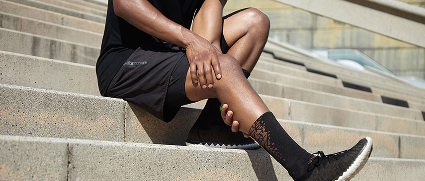 Person sitting on outdoor stairs wearing athletic shorts and lace-up sneakers, taking a break to evaluate common running injuries.