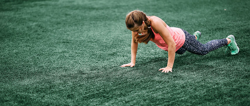 Young girl spice up your routine by doing push-ups on a grassy field.