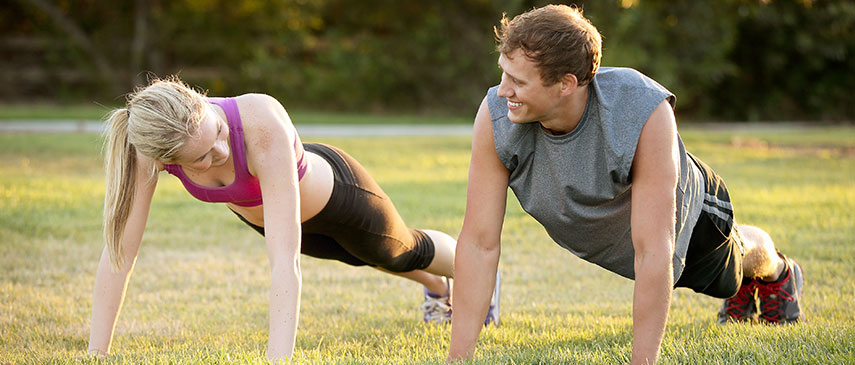 Two people performing interesting workouts, doing push-ups outdoors at sunset.