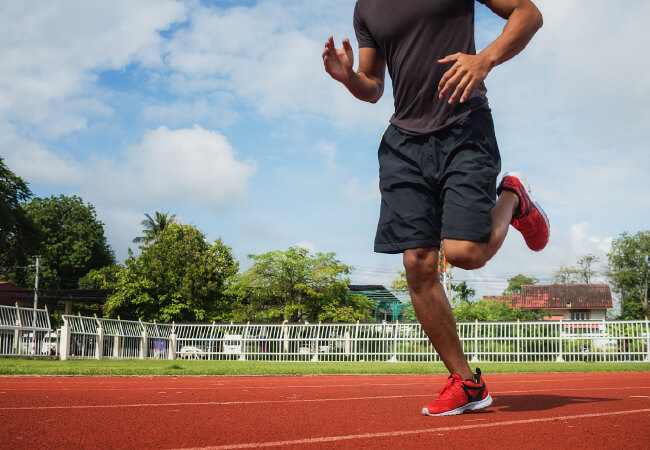 A person jogging on a red running track, focusing on their lower body for health and fitness improvement.