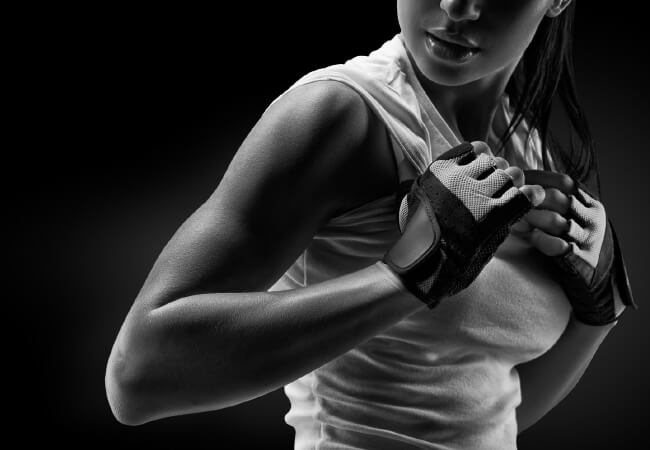 A close-up of a woman in workout attire wrapping her shoulder and hand with sports tape to enhance her strength.