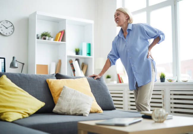 Woman experiencing back pain and dizziness while standing in a living room.