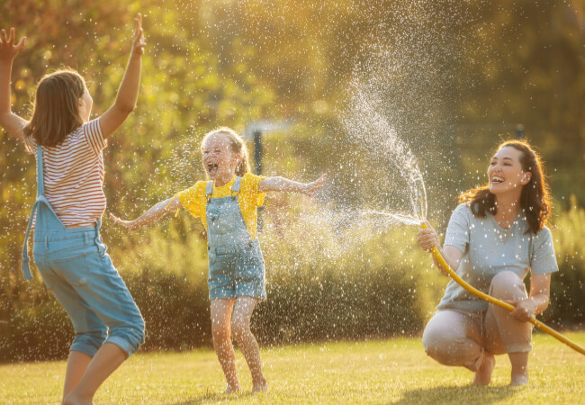 Three people enjoying a sunny day with a water hose in a garden, one of them managing chronic pain with a smile.