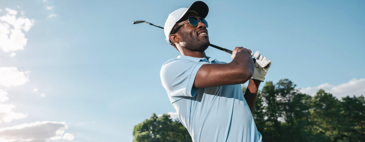 Golfer in mid-swing on a sunny day, practicing after a physical therapy session.