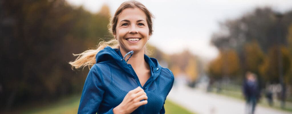 Woman jogging in a park with autumn trees in the background, mindful of preventing running injuries.