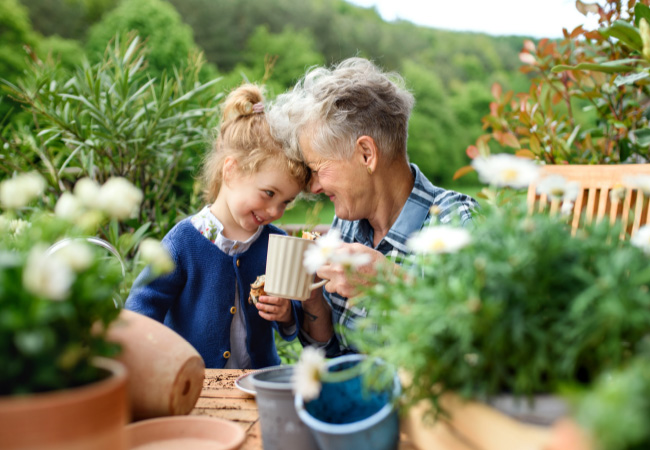 A grandmother and granddaughter enjoy gardening together, sharing a moment of connection amidst potted plants, while also focusing on techniques to prevent gardening injuries.