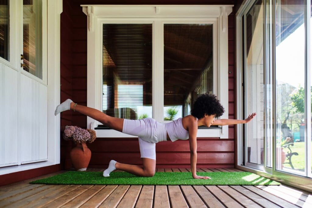 Woman practicing regular stretching exercises in a yoga pose on a porch, experiencing amazing benefits.