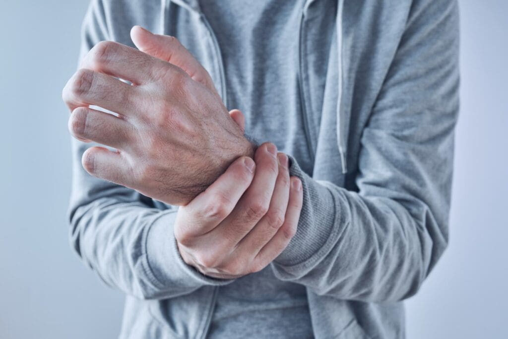 A person cradling their wrist, possibly indicating pain or discomfort, seeking relief strategies for arthritis pain.