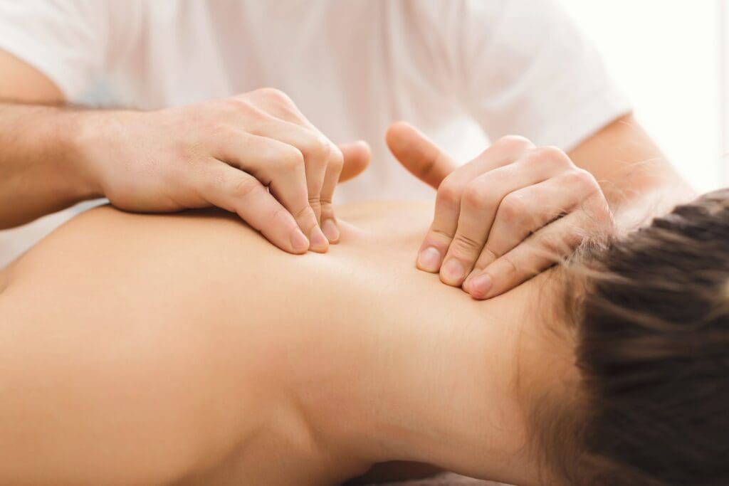 A therapist performing a back massage on a client with herniated discs in a bright room.