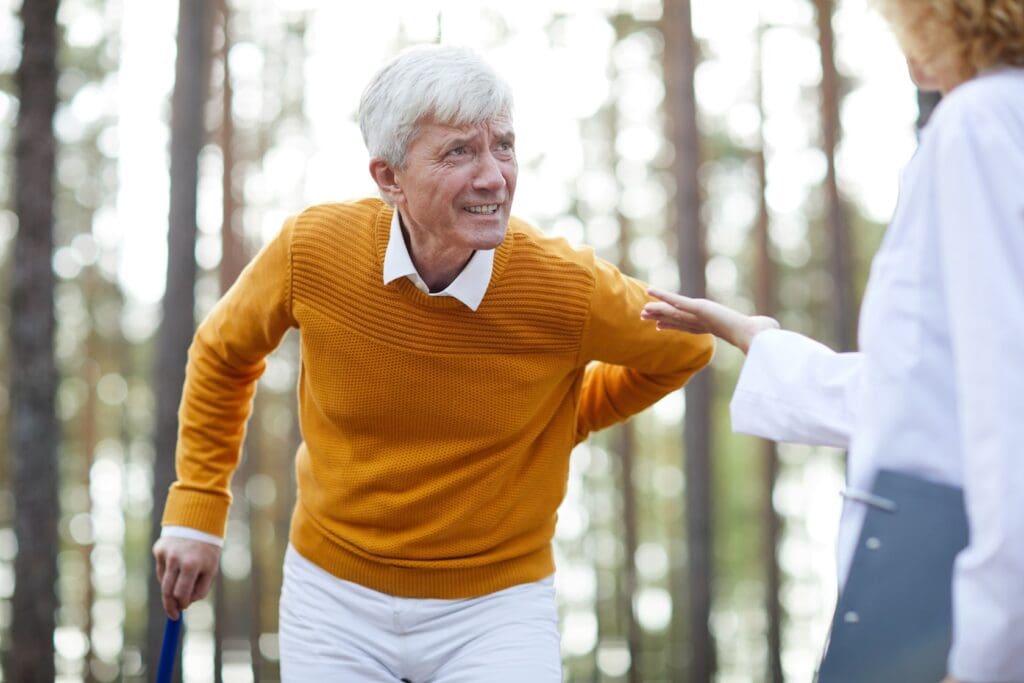 Elderly man with a cane walking in the forest, assisted by a healthcare professional focusing on rehabilitation strategies.