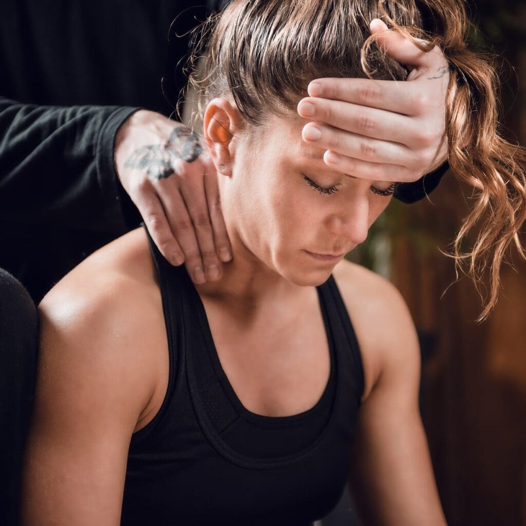 A therapist applies kinesiology tape to the shoulder of a woman experiencing work-related aches while she sits and looks down.